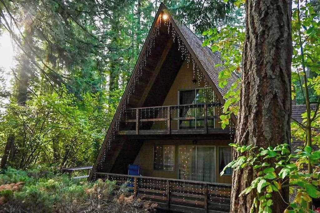 Eine Hütte mit geneigtem Dach, einem Balkon und einer Terrasse, umgeben von Bäumen.