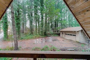 A view through a triangular window of a forested area with a gravel driveway leading to a garage. - 2BR cabin with loft in wooded setting with WiFi (Beaverton)