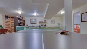A room with a ping pong table, a bookshelf, and a kitchen area. - Cheery 2BR Golf Course View Oregon Wine Country (McMinnville)