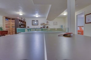 A room with a ping pong table, a bookshelf, and a kitchen area. - Cheery 2BR Golf Course View Oregon Wine Country (McMinnville)