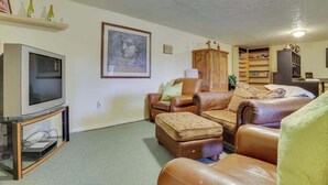 A living room with a television, leather sofas, a cabinet, and a bookshelf. - Cheery 2BR Golf Course View Oregon Wine Country (McMinnville)