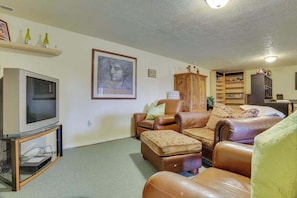 A living room with a television, leather sofas, a cabinet, and a bookshelf. - Cheery 2BR Golf Course View Oregon Wine Country (McMinnville)
