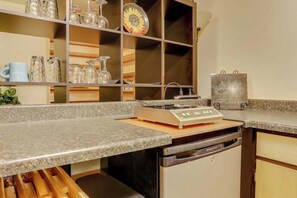 A kitchen with a built-in stove, a dishwasher, and a shelf with glassware and a decorative plate. - Cheery 2BR Golf Course View Oregon Wine Country (McMinnville)