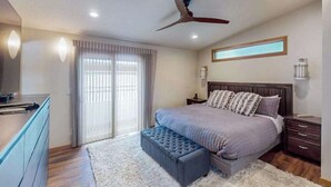 Ein Schlafzimmer mit Bett, Deckenventilator, Nachttisch, Kommode und einem Fenster mit Vorhängen.