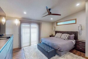 A bedroom with a bed, a ceiling fan, a nightstand, a dresser, and a window with curtains. - Delightful 2BR Lakefront - Patio (Lake Oswego)