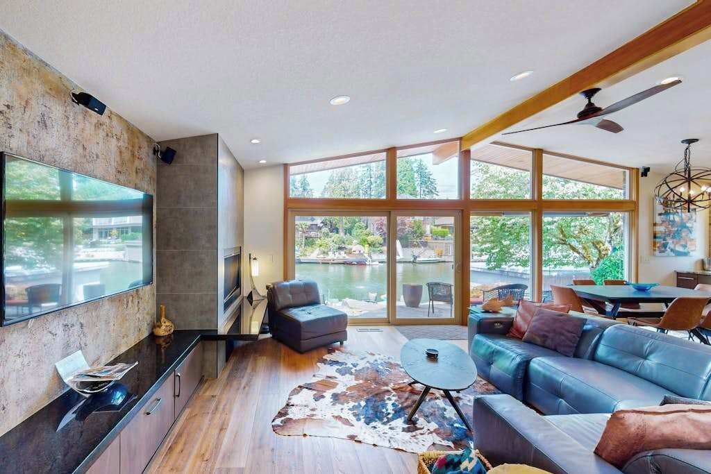 Un salón moderno con televisor grande, asientos cómodos y vista a un cuerpo de agua.