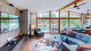 Ein modernes Wohnzimmer mit großem Fernseher, bequemen Sitzmöglichkeiten und Blick auf ein Gewässer.