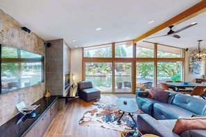 A modern living room with a large TV, comfortable seating, and a view of a body of water. - Delightful 2BR Lakefront - Patio (Lake Oswego)