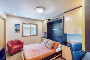 A bedroom with a bed, a red chair, a desk, and a wardrobe. - Delightful 2BR Lakefront - Patio (Lake Oswego)