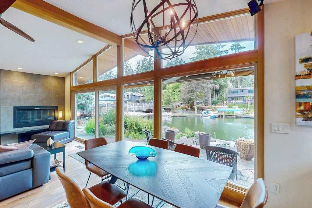 A modern living room with a large dining table, comfortable seating, a television, and a view of a lake with boats.