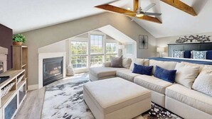 Un salon spacieux avec un haut plafond, une cheminée, un grand ensemble de canapés et un ventilateur de plafond.