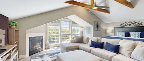 A spacious living room with a high ceiling, a fireplace, a large sofa set, and a ceiling fan.