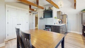 Une cuisine moderne avec des poutres en bois, une table à manger avec des chaises et un îlot central intégré doté d’un évier.