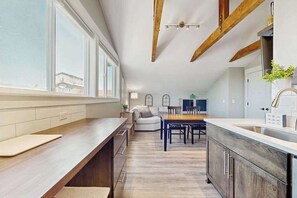 A modern kitchen with a long counter, wooden beams, and a dining area with a table and chairs. - High-End Rooftop Studio Oregon Wine Country (McMinnville)