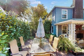 Eine Terrasse im Freien mit Tisch und Stühlen, umgeben von Grünpflanzen und einem Haus.