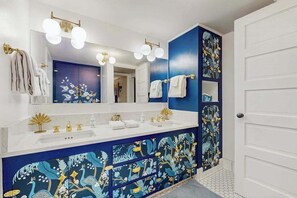 Ein Badezimmer mit weißem Waschtisch, einem großen Spiegel und einer blauen Wand mit floralem Dekor.