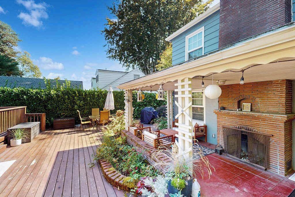 A wooden deck with a brick fireplace, outdoor seating, and a garden area.