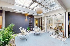 Ein moderner Außenbereich mit zwei weißen Stühlen, einer Glastür zu einem Wohnraum und einem Oberlicht darüber.