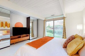 A modern bedroom with a large bed, a flat-screen TV, a mirror, and a window with curtains. - MCM 3BR atrium & yoga room near Nike HQ & shopping (Portland)
