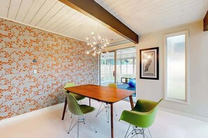 Ein moderner Konferenzraum mit einem Holztisch, grünen Stühlen, einer Deckenleuchte und einer Wand mit einem floralen Muster.