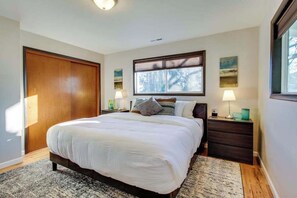 Une chambre à coucher avec un grand lit, une armoire en bois, une table de chevet avec une lampe et une fenêtre avec des stores.