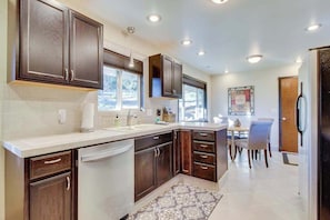 A modern kitchen with dark wood cabinets, a white countertop, and a dining area with a table and chairs. - Wine Country 3BR Mountainview Oregon Wine Country (Dundee)