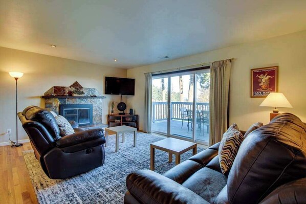 A living room with a fireplace, a sofa, a television, and a view through a sliding glass door. - Wine Country 3BR Mountainview Oregon Wine Country (Dundee)