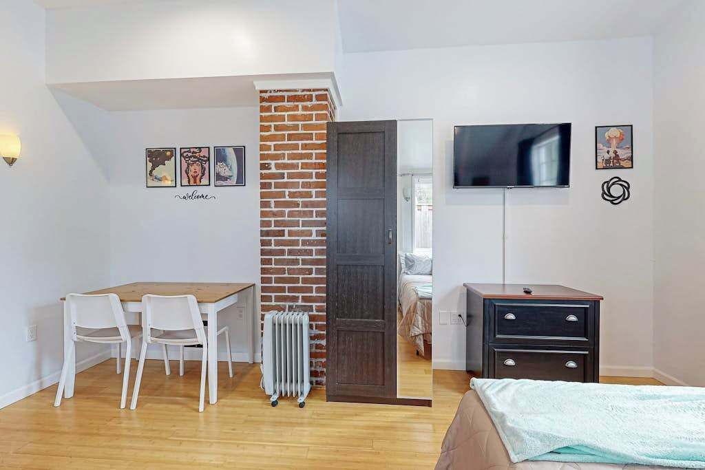 Una habitación con cama, un escritorio y sillas, un radiador, televisión y obras de arte en las paredes.