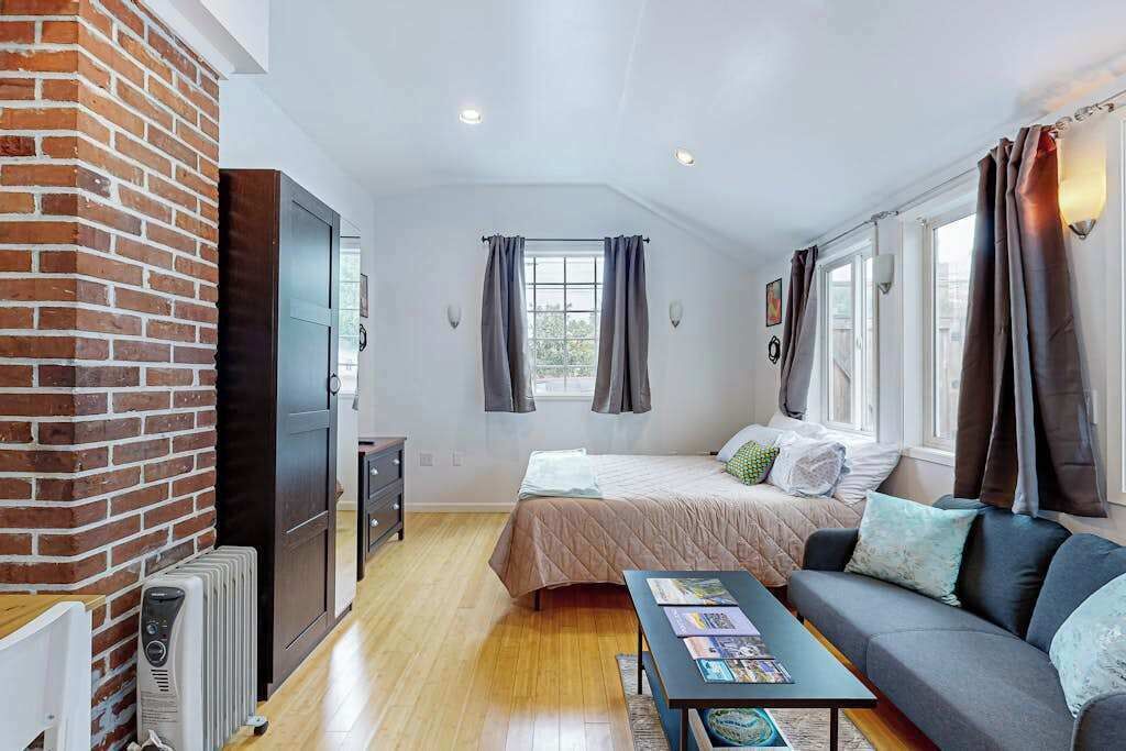 Een kleine kamer met een bed, een bank, een tafel, een radiator en een bakstenen muur.