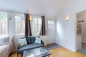 Una habitació amb un sofà, una taula de cafè amb revistes, una porta amb un rètol i una finestra amb cortines.
