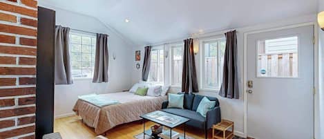 A compact room with a bed, a sofa, a small table, and a door.