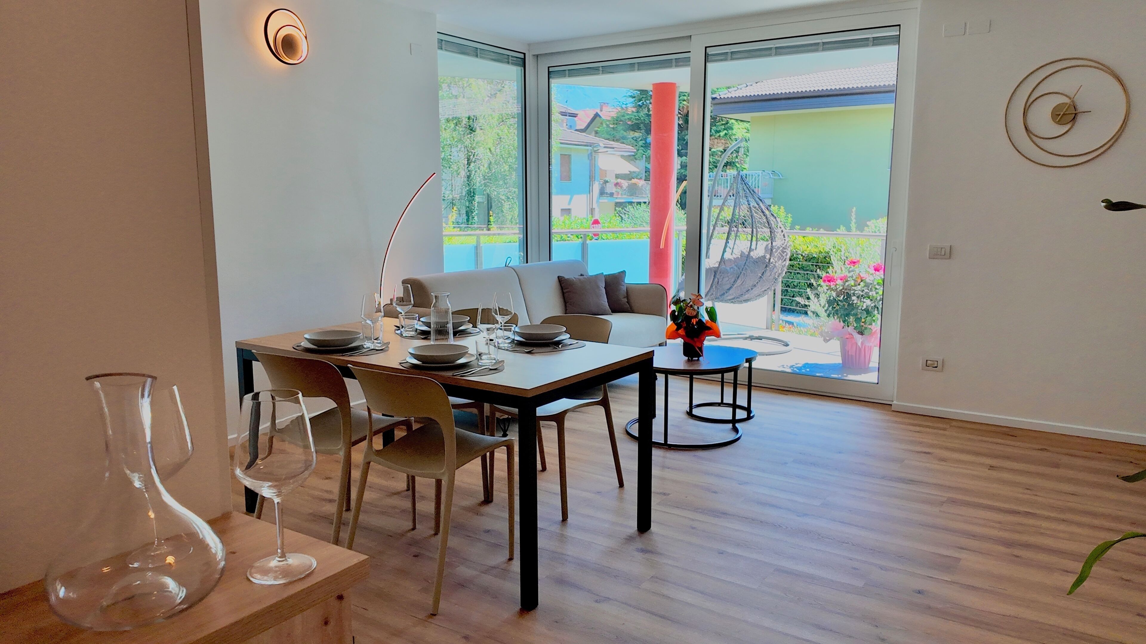 Een eetruimte met een tafel gedekt voor vier personen, een bank en uitzicht op een tuin door grote ramen.