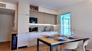 A compact kitchen with a built-in oven, a coffee machine, and a sink. There is a dining table with chairs and a view of the outdoors through a glass door. - Residenza Francesca Luxury Suite (Riva del Garda)