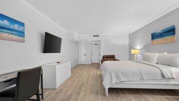 Habitación de hotel con cama, escritorio, silla, televisor y obras de arte en las paredes.