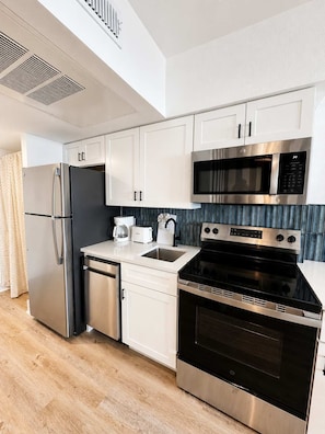A modern kitchen with stainless steel appliances, white cabinetry, and a blue backsplash. - Boardwalk Noir - Oceanfront Studio Yachtsman 404 (Myrtle Beach)