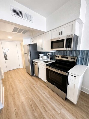Cocina compacta con armarios blancos, refrigerador de acero inoxidable, microondas, estufa y lavavajillas.