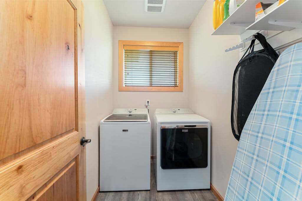 A compact laundry room with two washing machines, a window with blinds, and a door.