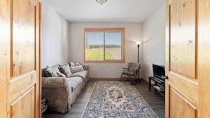 Ein Zimmer mit einer Couch, einem Fernseher, einer Lampe und einem Fenster mit Jalousien.