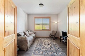 Ein Zimmer mit einer Couch, einem Fernseher, einer Lampe und einem Fenster mit Jalousien.