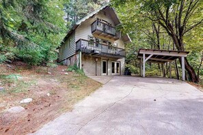 Eine zweistöckige Hütte mit einem Balkon, einer Veranda und einer Auffahrt, die zum Eingang führt.
