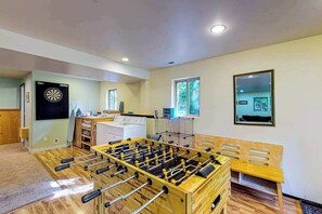 Una habitació amb taula de futbolí, dardo i zona de cuina amb fogó i nevera.