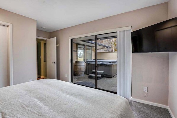 Habitación de hotel con cama, puerta corrediza de vidrio que da a un balcón y televisor de pantalla plana montado en la pared.