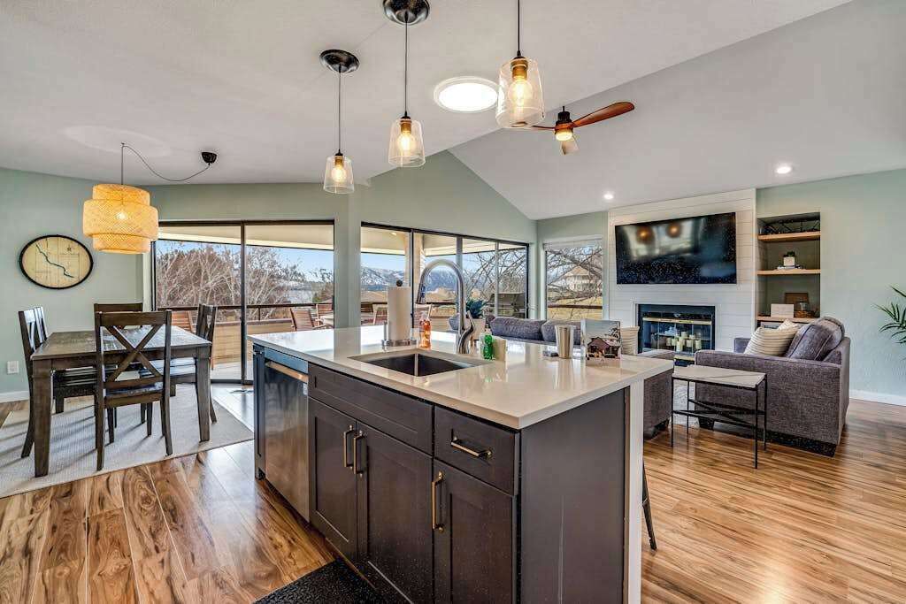 A modern kitchen with a large island, dining area with chairs, and a living room with a sofa and fireplace.