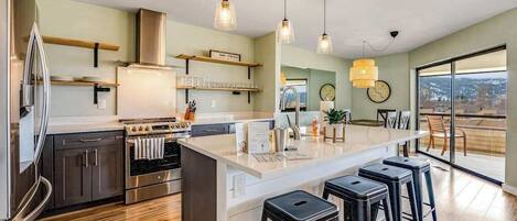 A modern kitchen with stainless steel appliances, a central island with stools, and a view through large windows.