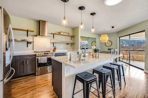 Una cocina moderna con electrodomésticos de acero inoxidable, una isla central con taburetes y vistas amplias a través de grandes ventanales.