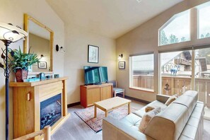 A living room with a fireplace, television, sofa, and large windows. - Downtown 1BR Mountainview 2nd-Floor - Balcony (Leavenworth)