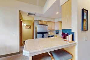 A compact kitchen with a built-in bench, a refrigerator, and wooden cabinets. - Downtown 1BR Mountainview 2nd-Floor - Balcony (Leavenworth)