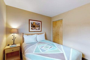 Un dormitorio con cama, una mesita de noche con lámpara, un cuadro enmarcado en la pared y un armario de madera.