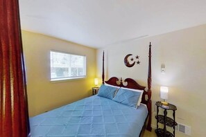 Un dormitorio con cama con dosel, una ventana con persianas, decoración de luna creciente y estrellas en la pared, y una mesita de noche con lámpara.