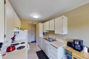 A compact kitchen with white cabinets, a stove, a sink, and a coffee maker. - 2BR Lakeview - Patio - Washer/Dryer (Chelan)